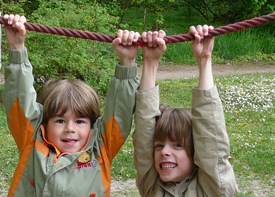 Zwei Kinder hängen auf dem Spielplatz an einem Seil.