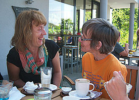 Zwei Frauen unterhalten sich in einem Café draußen auf einer Terrasse.