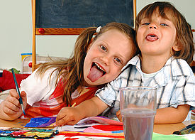 Ein Junge und ein Mädchen malen mit Wasserfarben und strecken der Kamera die Zunge raus.