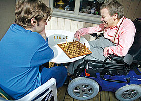 Ein Mann im Rollstuhl spielt mit einer Assistenzkraft Schach.