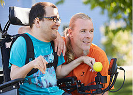 Ein Mann im Rollstuhl unterhält sich mit einem Betreuer draußen in einem Garten.