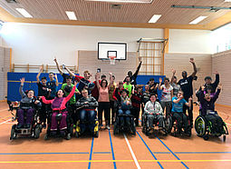 Eine Gruppe Jugendlicher und einige Sportler stehen in einer Sporthalle und winken.