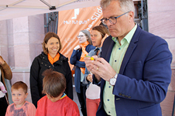 Rastatts Oberbürgermeister Hans Jürgen Pütsch steht am Stand der Reha-Südwest und bemalt einen Teil der Inklusions-Skulptur zusammen mit Kindern und Reha-Südwest-Geschäftsführerein Mirjam Weisserth.