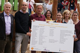 Sieben Personen halten eine Tafel, auf der die Namen der Spender für die Kita Rosengarten aufgelistet sind.