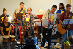 Eine Gruppe von acht jungen Musikern steht mit Instrumenten auf einer Bühne.