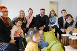 Sieben Erwachsene und drei Kinder sitzen auf dem Boden mit Musikinstrumenten.