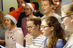 Junge Männer und Frauen singen im Chor. Drei von ihnen tragen Nikolausmützen.