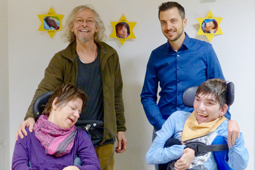 Vier Personen, davon zwei im Rollstuhl, stehen vor einer Wand.