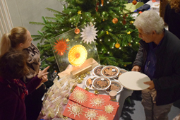 Ein Mann steht vor einem Verkaufsstand mit Torten, Plätzchen und Strohsternen. Im Hintergrund steht ein geschmückter Weihnachtsbaum.