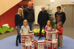 Vier Erwachsene und drei Kinder stehen hinter einem großen Spielhaus, das wie eine Burg gestaltet ist.