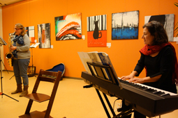 Eine Pianistin und eine Saxofonistin spielen ein Stück. Im Hintergrund hängen bunte Bilder an der Wand.