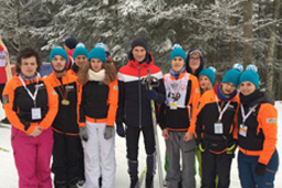 Eine Gruppe Schüler in Jacken und Mützen und ein Mann stehen im Schnee vor einem Tannenwald.