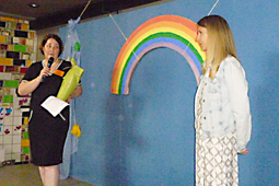 Zwei Frauen stehen auf einer Bühne, hinter ihnen befindet sich ein großer Regenbogen aus Pappe.
