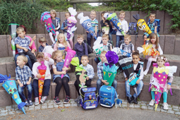 Eine Gruppe Schüler mit bunten Schulranzen und Schultüten sitzt auf einer Treppe.