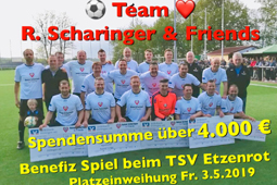 Ein Fußball-Team steht auf einem Fußball-Feld. Die Männer in der vorderen Reihe halten Spenden-Schecks.