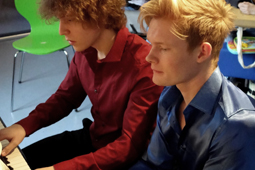 Zwei junge Männer spielen zusammen Klavier.