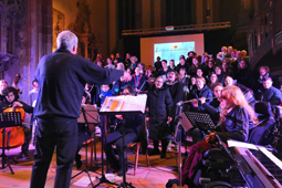 Ein Dirigent dirigiert einen Chor und Musiker im Innenraum einer Kirche.