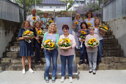 Mitarbeiter und Mitarbeiterinnen mit langjähriger Betriebszugehörigkeit haben sich für das Foto um eine Rutsche herum aufgestellt. In den Händen halten Sie Blumensträuße mit Sonnenblumen.