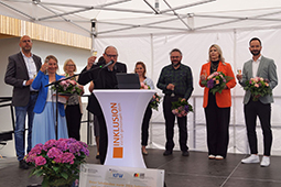 Auf einer Bühne stehen Männer und Frauen mit Blumensträußen und Sektgläsern.