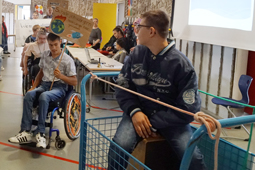 In einer Turnhalle sind mehrere Schüler zu sehen. Ein Junge im Rollstuhl hält ein Plakat hoch.