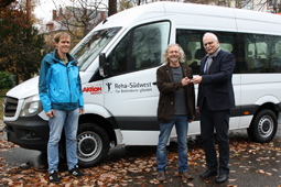 Drei Personen stehen vor einem Kleinbus mit der Aufschrift Reha-Südwest.